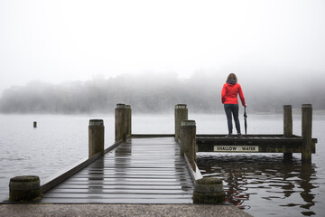 Woman in red from behind overlooking misty fogy view after hike walk outdoors on overcast day