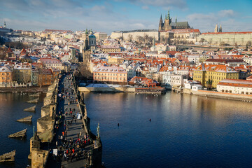 Obraz premium Aerial panoramic view from Old Town Bridge Tower, Karlov or Charles bridge and Vltava River in winter, sunny day, snow lies on red tiled roofs, Prague, Czech Republic