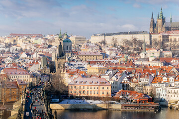 Fototapeta na wymiar Aerial panoramic view from Old Town Bridge Tower, Karlov or Charles bridge and Vltava River in winter, sunny day, snow lies on red tiled roofs, Prague, Czech Republic