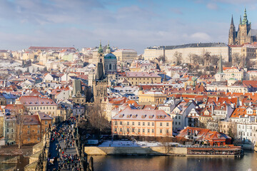 Fototapeta na wymiar Aerial panoramic view from Old Town Bridge Tower, Karlov or Charles bridge and Vltava River in winter, sunny day, snow lies on red tiled roofs, Prague, Czech Republic