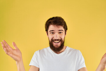 Bearded man emotions fun gesture with hands white t-shirt close-up yellow background