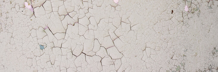Peeling paint on the wall. Panorama of a concrete wall with old cracked flaking paint. Weathered rough painted surface with patterns of cracks and peeling. Panoramic texture for background and design.