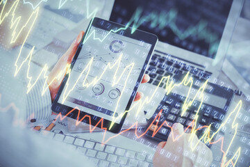 Double exposure of man's hands holding and using a digital device and forex graph drawing. Financial market concept.