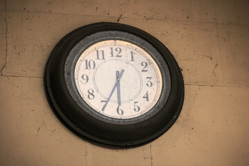 Old dirty round black outdoor clock on yellow wall