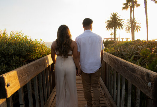 couple walking down bridge beach sunset