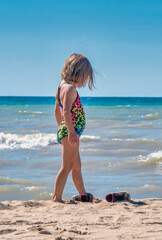 A barefoot child kicks off her shoes and digs her toes into the warm sand on the beach