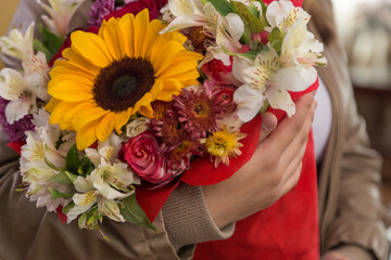 person in leather jacket holding beautiful and colorful bouquet of flowers with a sunflower, roses and different types of flowers, in a room, detail of the petals and leaves, nature