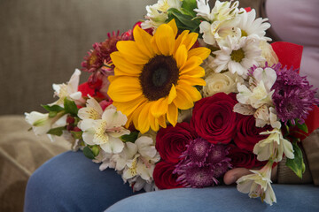 closeup of person in a sofa holding colorful bouquet of flowers with a sunflower and roses, romantic details, nature