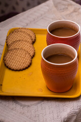 Two cups of milk tea on a with some biscuits