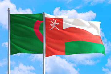Fototapeta na wymiar Oman and Algeria national flag waving in the windy deep blue sky. Diplomacy and international relations concept.