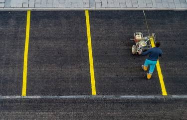 A worker is drawing outdoor concrete car parking lot is divided for making a slot for the park each car by a yellow line, with cement wheel coverings. in urban city. - obrazy, fototapety, plakaty