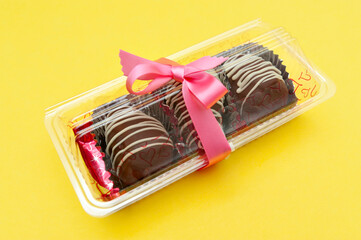 Delicious homemade chocolate bonbon packed for gift with red ribbon. Isolated on yellow background. Copy space.
