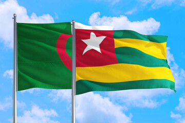 Togo and Algeria national flag waving in the windy deep blue sky. Diplomacy and international relations concept.