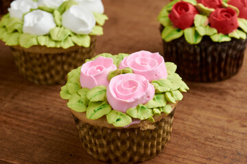 cupcake decorated with chantilly with rose design, placed on a wooden base, diffuse background of more cupcake
