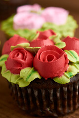 cupcake decorated with chantilly with rose design, placed on a wooden base, diffuse background of more cupcake