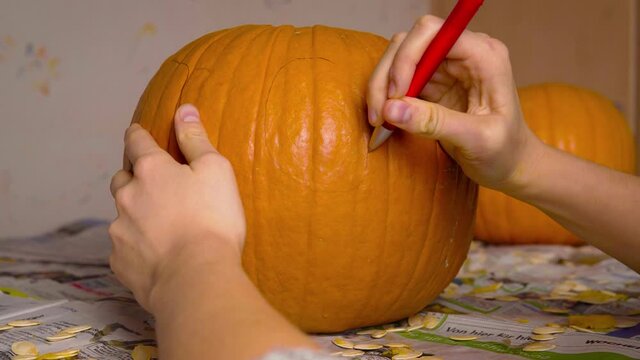 Pumpkin Carvin Female Drawing Cute Face of Jack O'Lantern onto Pumpkin with Pen getting ready to carve Halloween decoration.