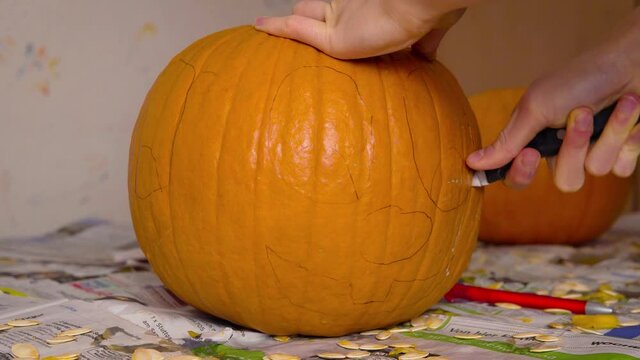 Pumpkin Carvin Female Cutting out Cute Face of Jack O'Lantern into Pumpkin with knife getting it ready as Halloween decoration.