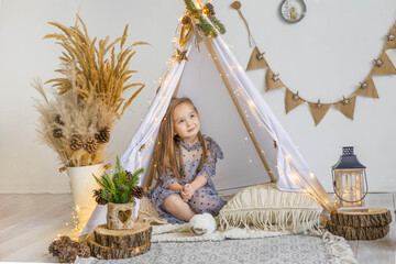 A cute little girl in a beautiful dress plays in a wigwam at home. New Year decoration. Merry christmas and happy new year concept © Наталья Мокрецова