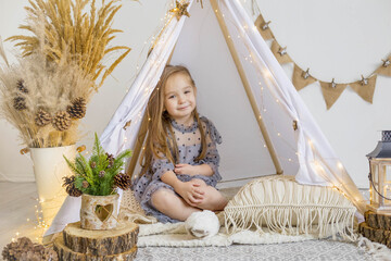 A cute little girl in a beautiful dress plays in a wigwam at home. New Year decoration. Merry christmas and happy new year concept © Наталья Мокрецова