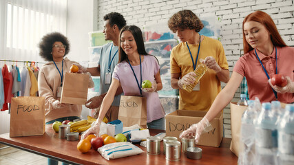 Young male and female volunteers packing food and drinks donation for homeless into boxes and paper...