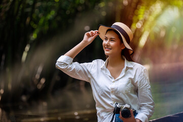 Adventure and vacation travel concept. Traveler young woman wearing hat and holding camera in her hand while sitting on the boat visit to see the tree tunnels feeling relax in the canal.