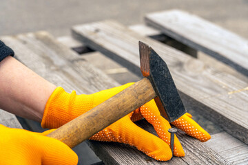 Orange-gloved hands hammer a nail into the board