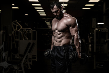 strong bearded male with dumbbells training in sport night gym