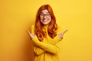 Positive redhead European woman crosses fingers and points at different sides picks two variants...