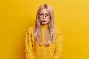 Adorable upset blonde European woman looks with gloomy expression looks offended and disappointed...
