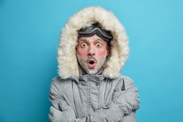 Stupefied frozen man with red face trembles from cold embraces himself to feel warm stares bugged...