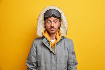 Stunned man snowboarder stares bugged eyes at camera wears warm winter jacket with hood has rest...