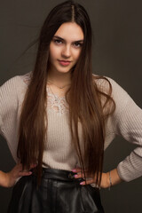 Young beautiful brunette with long hair, hands on her belt. In Studio photo on a dark background in warm colors