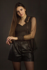 Young beautiful brunette with long hair, posing in black clothes. In a Studio photo