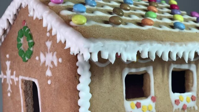 Reveal of a ginger bread house made with honey and flour with Christmas decorations with candies and white snow like decoration. Chrismtas decorated gingerbread house over defocused light background.