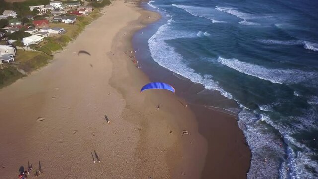 Aerial following a powered paraglider flying over a beach in summer