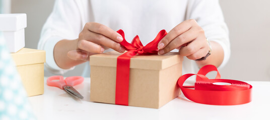 Closeup hand making present gift box with red ribbon for christmas and birthday present
