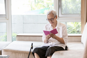 Smiling asian senior woman holding opened book,reading her personal diary notes,feeling happy at home alone,old elderly in spectacles,enjoying the old stories written in her life and good memories