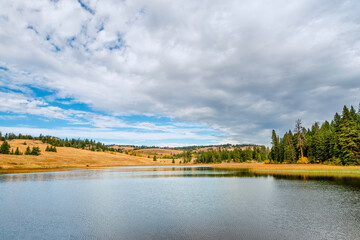 Fototapeta na wymiar Lake near yellow hills and green forest on a sunny autumn day