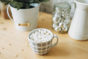 White cup with cacao or coffee with marshmallow on kitchen table, christmas mood, cozy home