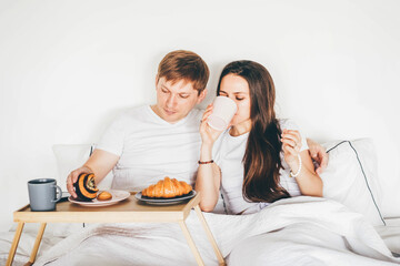 Lazy morning in bed. Lovely couple having breakfast on bed.