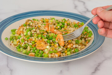 Blend of couscous, orzo, garbanzo beans, red quinoa cooked with shrimps and served with green peas and green onion close up on a plate on white background