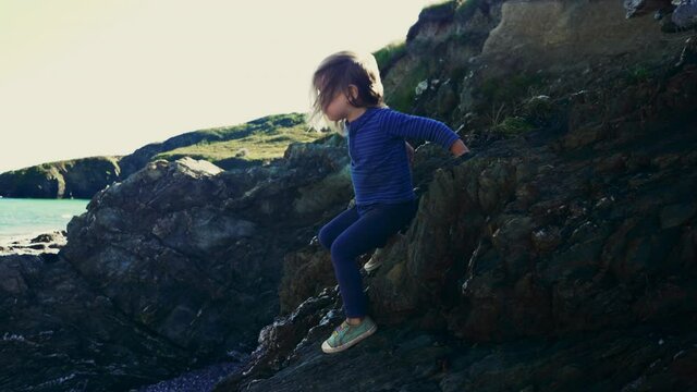 A little preschooler is climbing the rocks on the coast in autumn