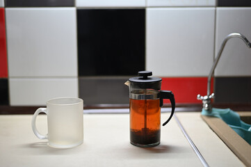 A photo of a teapot with tea with an empty mug is on the table in the kitchen.