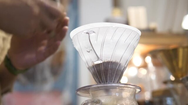 Barista preparing pour-over coffee with hand grinder and dripper in cozy caf&eacute;