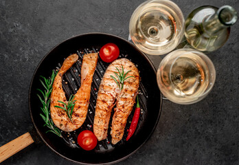 Dinner for two. Salmon steaks in a grill pan, a bottle of white wine and glasses on a stone background.
View from above