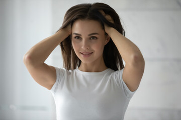 Thick and healthy. Long-haired millennial woman standing by mirror burying hands to her lovely shiny hair, female client is satisfied by result of regular use of professional beauty haircare products