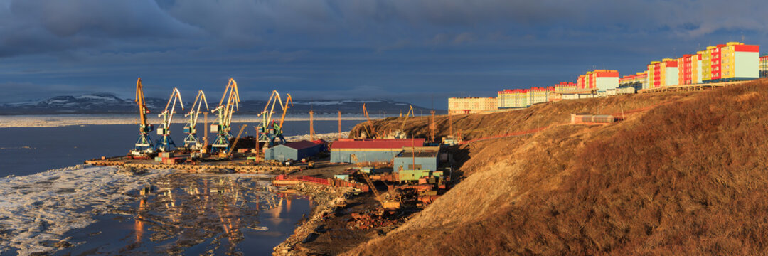 Beautiful panorama of a port town in the Arctic. View of the cargo seaport and colorful residential buildings. Melting ice in early summer in the Arctic. Anadyr, Chukotka, Siberia, Far East of Russia.