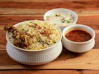 Traditional Hyderabadi Chicken dum Biryani made of Basmati rice cooked with masala spices, served with Onion raita and Salan, selective focus