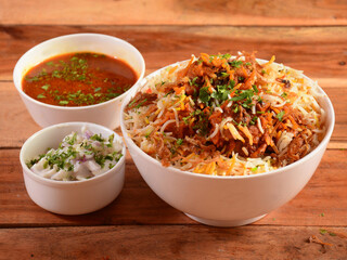 Traditional Hyderabadi Chicken dum Biryani made of Basmati rice cooked with masala spices, served with Onion raita and Salan, selective focus