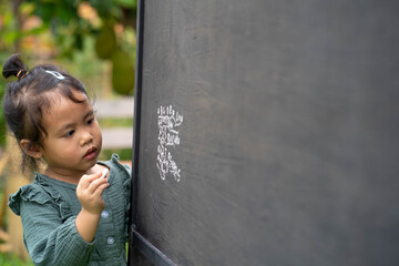 Cute little girl writing alphabet on blackboard in garden.